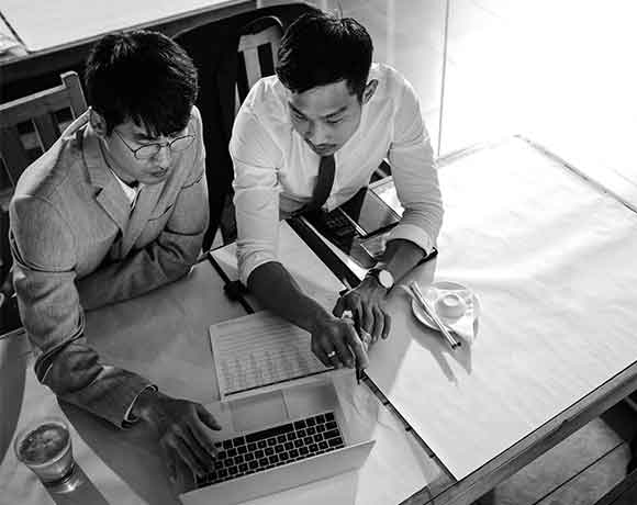 two manufacturing colleagues review product cost in black and white