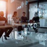 Two women and three men sitting in a conference room with digital graphics all around them discussing finances