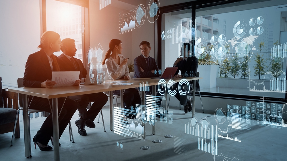 Two women and three men sitting in a conference room with digital graphics all around them discussing finances